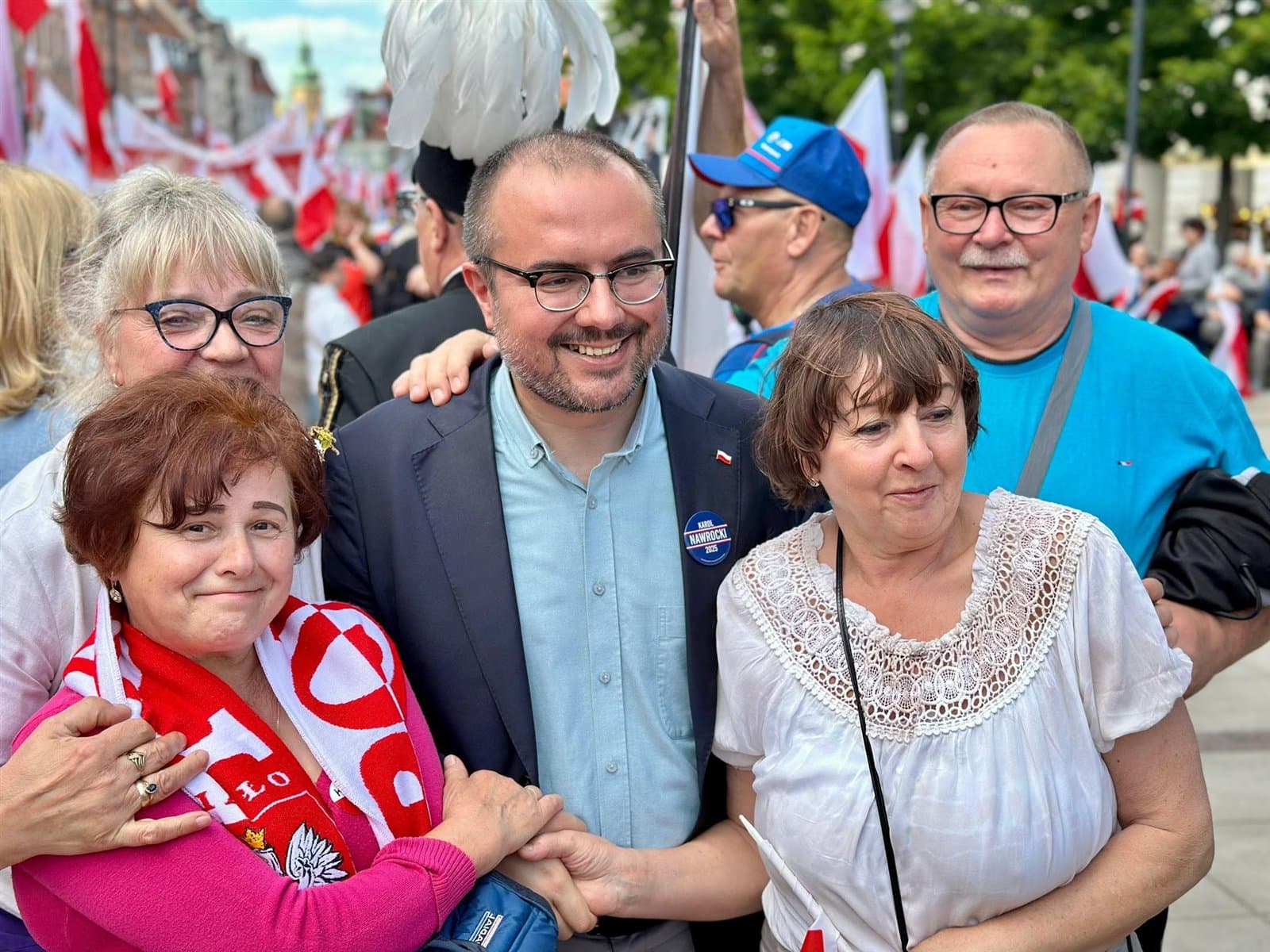 Paweł Jabłoński ściska dłoń uczestniczki marszu, wokół uśmiechnięci ludzie z biało-czerwonymi flagami